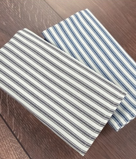 Two Napkin Craft Collection 100% Poly Smoky Blue napkins by 1Concier, featuring vertical blue and black stripes, are neatly folded and displayed on a wooden surface.
