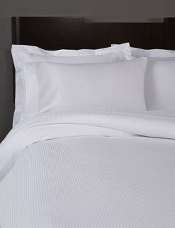 A neatly made bed with white pillows in 1Concier Pillow Case T300 100% Cotton (5mm Stripe), set against a dark headboard and complemented by luxurious Micro-Stripe sheets.