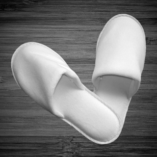 Two white 1Concier Slippers boxer Boxer Closed slippers are arranged in a heart shape on a dark wooden floor.