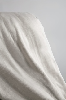 The 1Concier Blanket Plush Blankets, in a light hue, create smooth, flowing folds as they drape softly against a gentle gray backdrop.