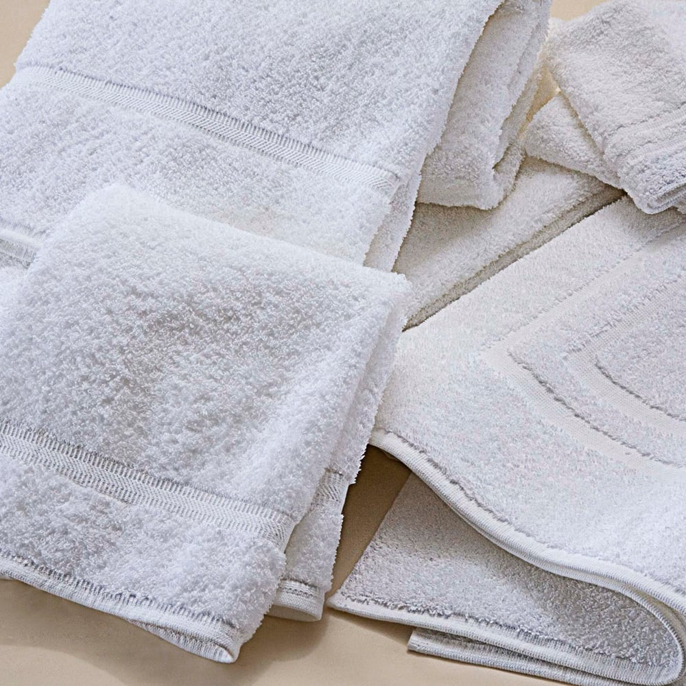 A set of neatly folded Martex Sovereign Dobby Towels by WestPoint Home lies on a light beige surface, featuring a soft, fluffy texture, simple decorative borders, and superior durability for lasting comfort.