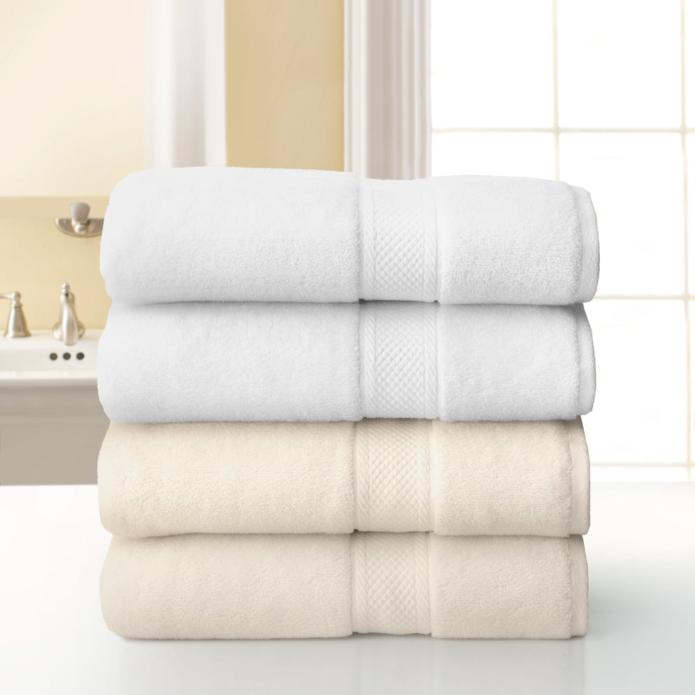 Four neatly folded Grand Patrician Suites Dobby Towels by WestPoint Home—two white on top, two beige below—are stacked on a white surface in a bright bathroom with a window and sink in the background.