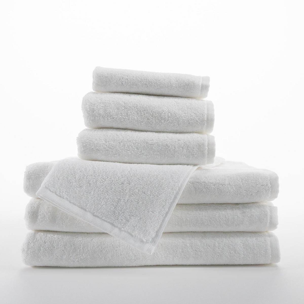 A stack of white Borderless Towel - Martex Luxe by WestPoint Home, made from 100% ring spun cotton, sits neatly on a white surface. The towels are fluffy, absorbent, and clean, with one towel draped over the stack.