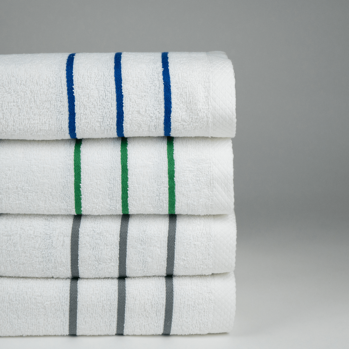 A stack of four Martex Cabana Collection Pool Towels by WestPoint Home—white with blue, green, and gray stripes—are neatly displayed on a gray background. Ideal for poolside or cabana relaxation.