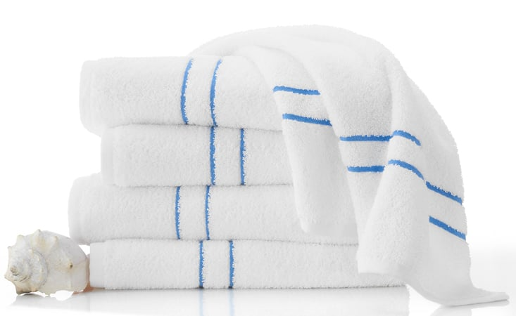 A stack of four WestPoint Home Martex Tropical Stripe pool towels, neatly folded with one draped over the top, sits beside a seashell on a white surface. Perfect for wholesale or updating your coastal decor.