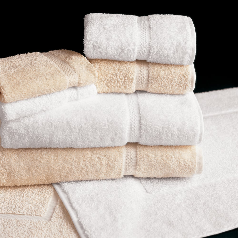 A stack of WestPoint Home Martex Brentwood Dobby Towels and washcloths, made from 100% cotton, are neatly folded on a matching white bath mat against a black background.