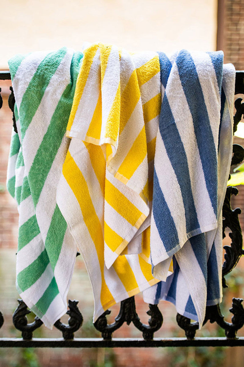 A Thomaston Mills White With Pineapple Yellow Stripe cotton towel hangs over a black wrought iron railing outdoors, highlighting its stylish look and durable quality.