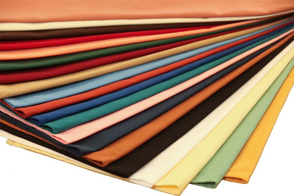 A semi-circular stack of Ganesh Mills Lapkins - Oversized Napkins in solid colors—brown, red, green, blue, pink, black, cream, yellow, and orange—ideal for bulk polyester napkin needs and beautifully arranged for display.
