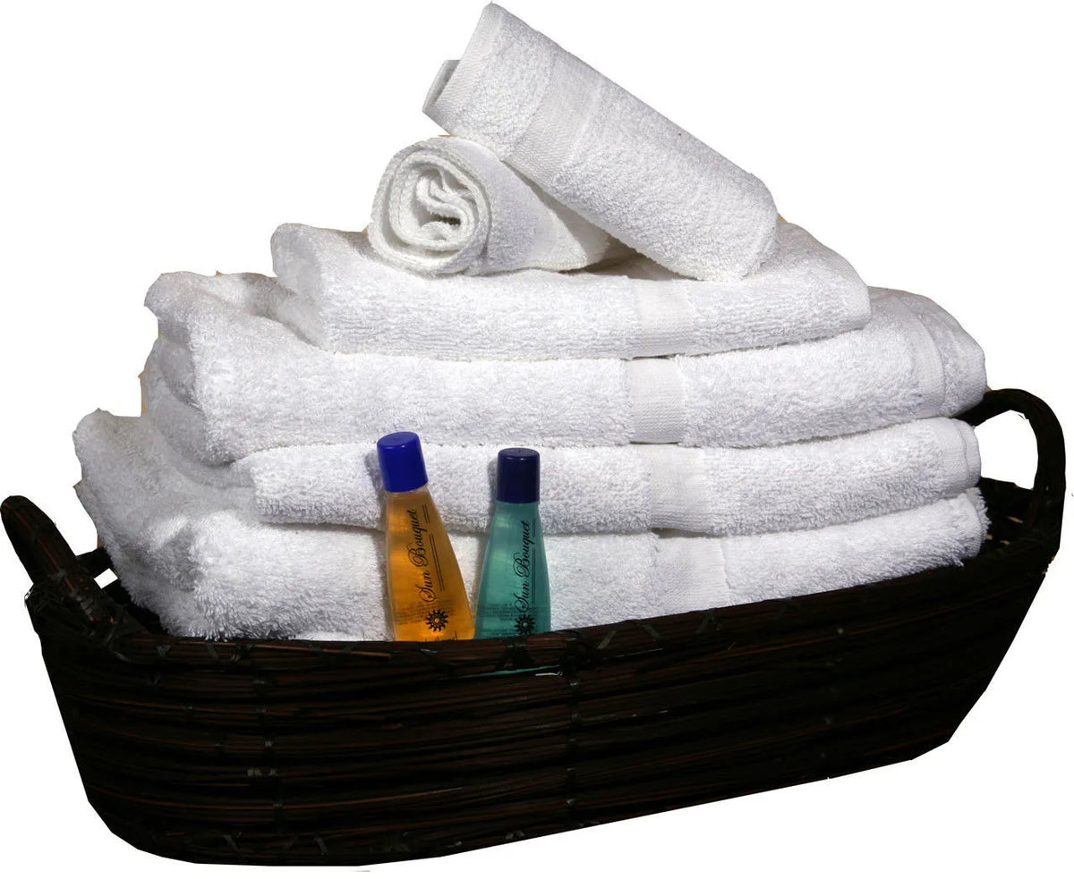 A dark wicker basket holds neatly folded Ganesh Mills Washcloths—White Oxford Classic Bronze Towels—with two small bottles of toiletries, one yellow and one blue, placed in front.