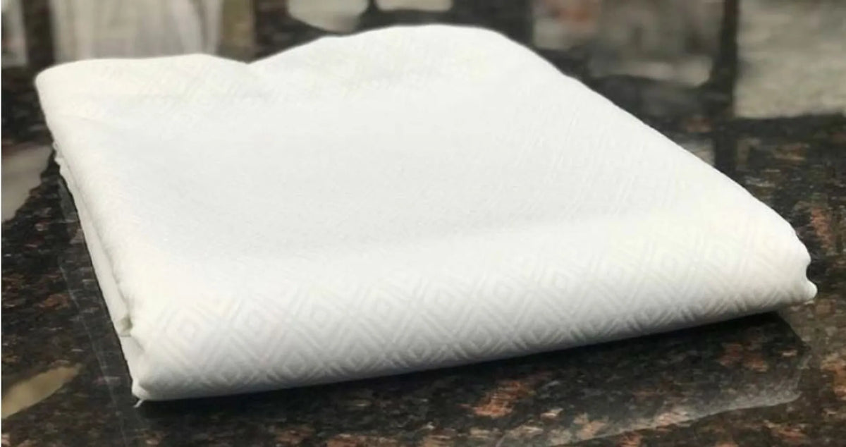 The Ganesh Mills Oxford Bed Topper - Jacquard Matelassé, featuring a subtle diamond pattern, is neatly folded and displayed on a polished dark granite countertop.