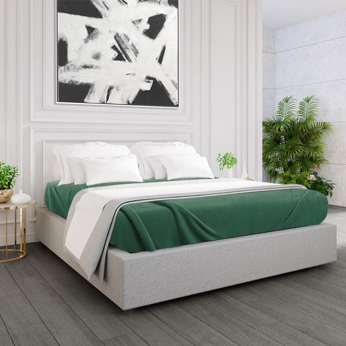 A modern bedroom features a low gray upholstered bed with Ganesh Mills Oxford Polar Fleece Blankets, anti-pilling and double stitched, in green and white, potted plants, light wood floors, and abstract black-and-white art on a paneled wall.