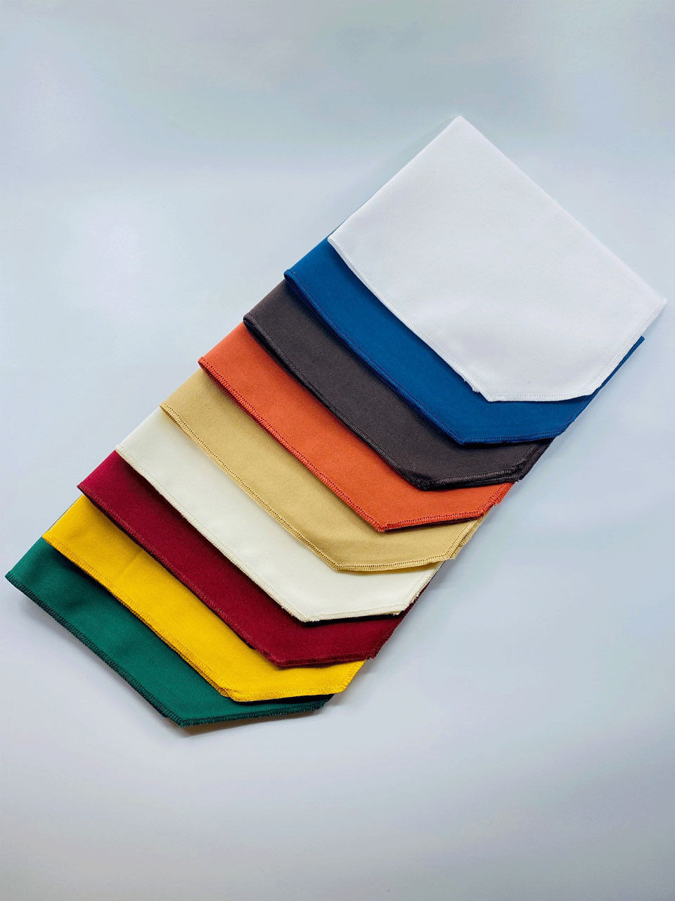 A set of Ganesh Mills Rectangular Octagon placemats, each in a bold solid color, is arranged diagonally in a neat stack, creating a vibrant and eye-catching display against a plain background.