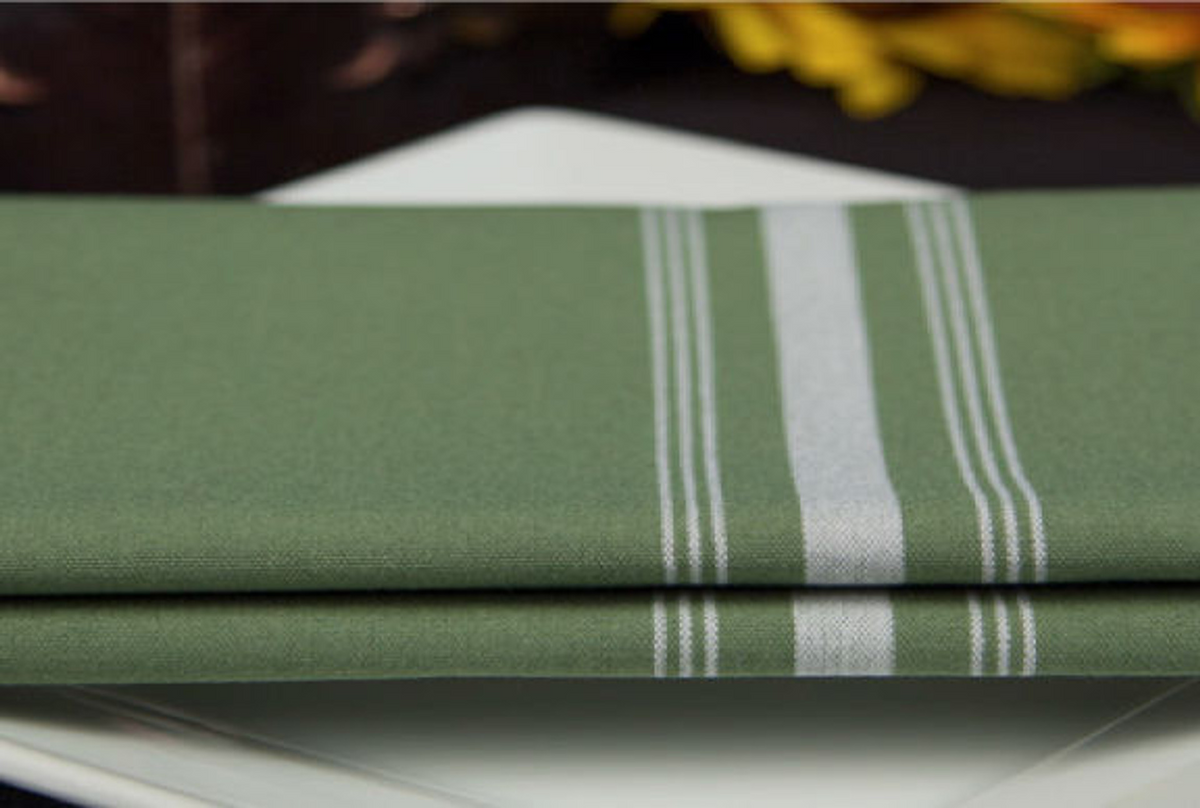 A Premier Bistro Napkin by 1Concier, featuring green with white stripes, is neatly folded on a white plate. The softly blurred background includes hints of yellow and dark tones.