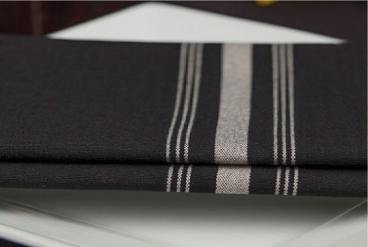 A close-up of folded Premier Bistro Napkins by 1Concier, featuring three parallel white stripes, displayed atop a stack of white plates.