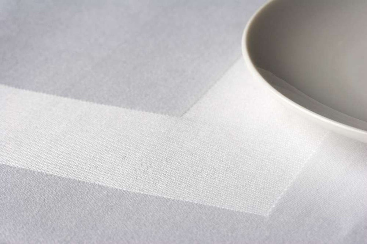 A close-up of a white plate set on Ganesh Mills’ Tablecloth - White Oxford Cotton Satin Band Table Linens, featuring a bold geometric stripe pattern beneath the plate.
