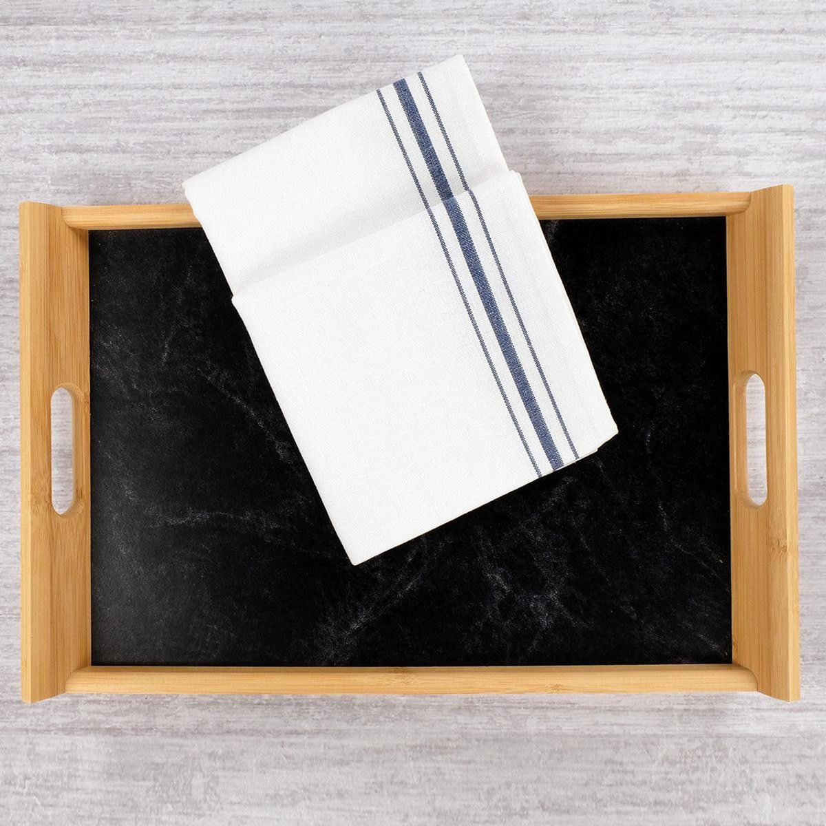 A wooden tray with a black base sits on a light gray textured surface. A 1Concier Napkin Bistro 100% Cotton White with Black Stripe is folded diagonally and placed on the tray.