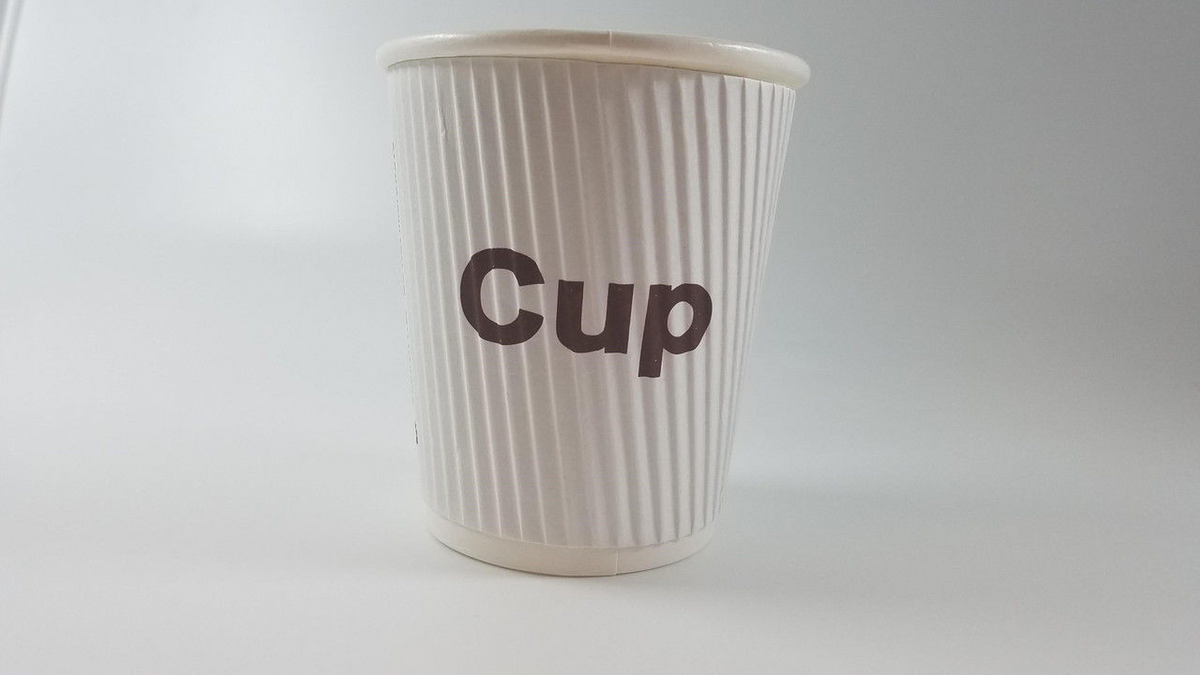 A Ganesh Mills 9 oz coffee cup with a white, ribbed paper design and “Cup” in bold brown letters on the front is paired with a Plastic Lid for 9 oz Coffee Cup Wholesale, set against a plain, light background.