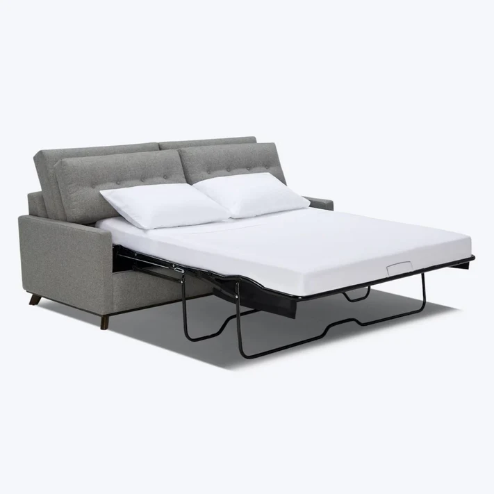 A gray upholstered sofa bed is unfolded to reveal a mattress dressed in Bargoose Sleeper Sofa Sheets T-360 100% Cotton and two white pillows, emphasizing its dual function as a stylish couch and a comfy pull-out bed.