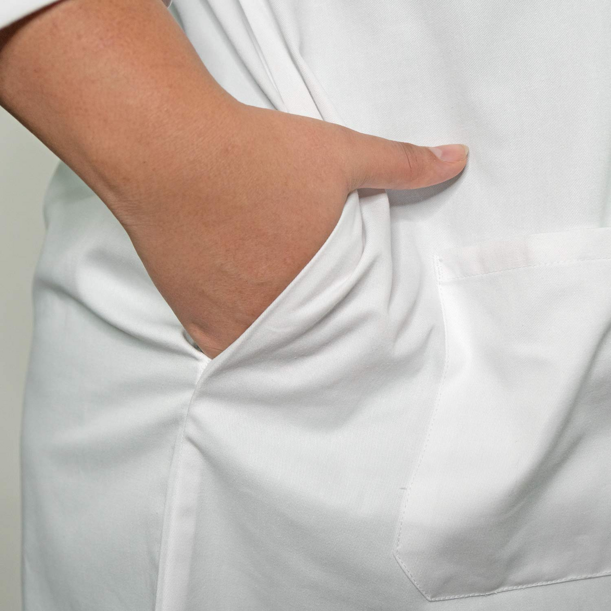 A person wearing a Martex Health Lab Coat by WestPoint Home places their hand in the front pocket; the image highlights the antimicrobial coat's pocket and arm area against a neutral background.