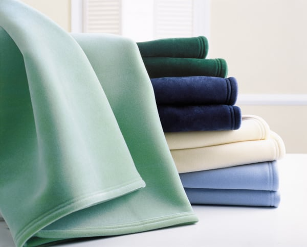 A stack of WestPoint Home Vellux Blankets in green, navy, cream, and light blue rests on a white surface with a pale background—ideal for anyone looking for cozy, wholesale blankets.