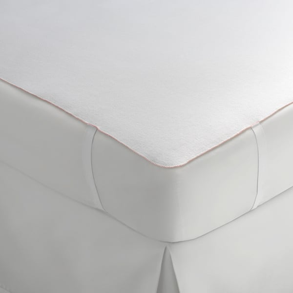 A close-up shows a neatly made bed featuring the WestPoint Home Mattress Pad - Martex Ultra Touch, with a crisp white fitted sheet and waterproof pad for smooth corners and a tailored look.