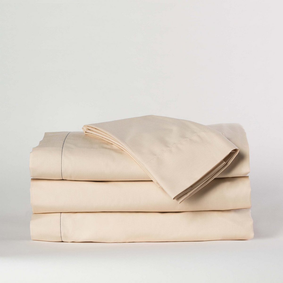 A cream Martex Millennium 250 flat sheet from WestPoint Home, made from a cotton-rich blend, is neatly folded with two pillowcases on top, all displayed against a plain white background.