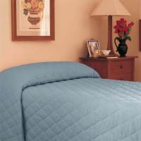 A neatly made bed with a light blue WestPoint Home Bedspread - Martex Mainspreads - Solid, featuring EcoPure polyester fiberfill, sits beside a wooden nightstand with a lamp, red flowers, framed photos, and floral artwork above the bed.
