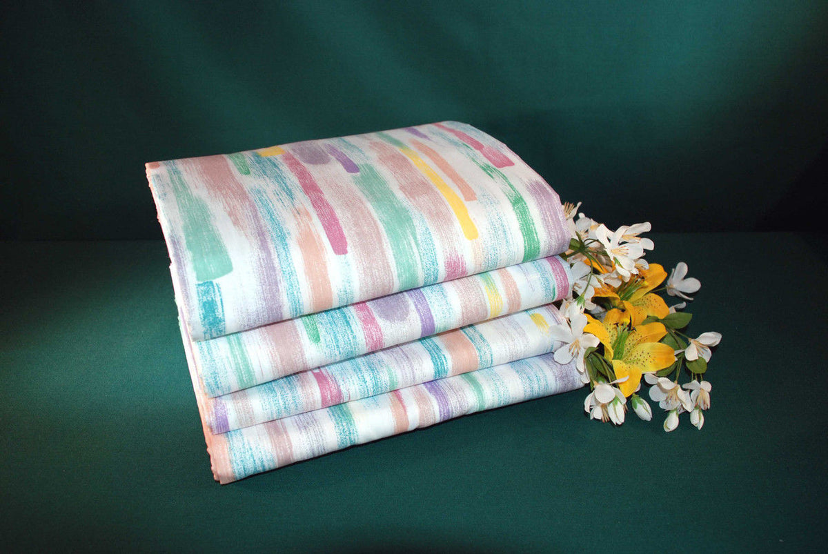 A stack of Thomaston Mills Crafted White Healthcare Items T-130 percale sheets, folded and set on a dark green surface beside a small bouquet of white and yellow flowers.