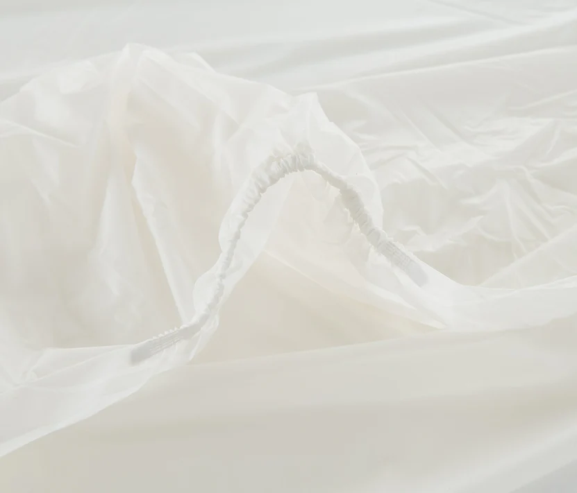Close-up of the Bargoose 6 Gauge Vinyl Fitted Waterproof Mattress Cover, 9 deep, shows its white elastic-edged fit spread flat. The gathered seam creates folds like those on a typical waterproof mattress protector.