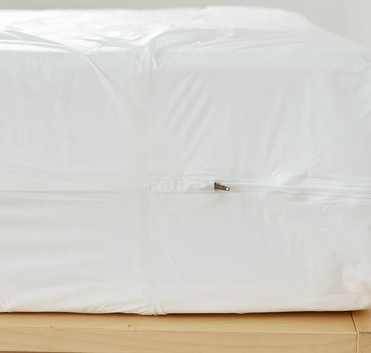 Close-up of a Bargoose 3 Gauge Vinyl Zippered Cover on a white mattress (fits up to 9 deep), showing side zipper. Provides waterproof protection and bed bug defense; shown on a wooden surface.