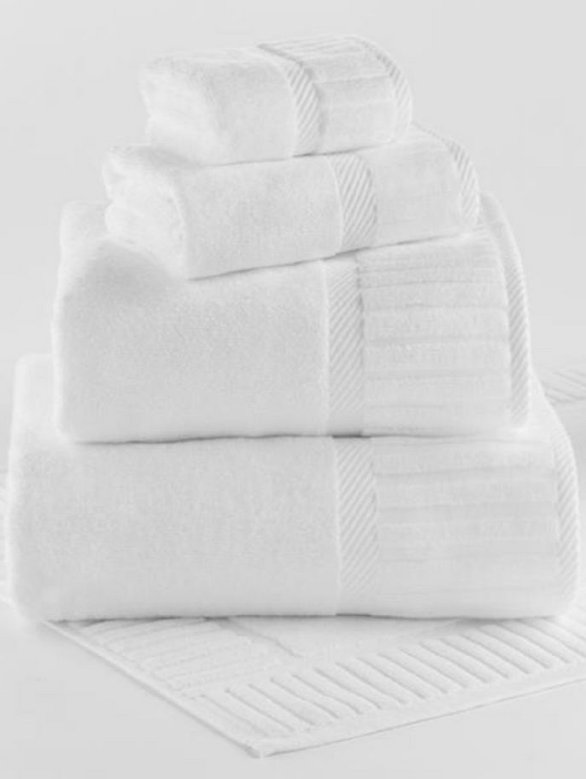 The 1Concier Bath Towel Terry Ensemble features four white 100% cotton towels in assorted sizes with subtle textured stripes, neatly stacked on a matching bath mat, all set against a clean white background.
