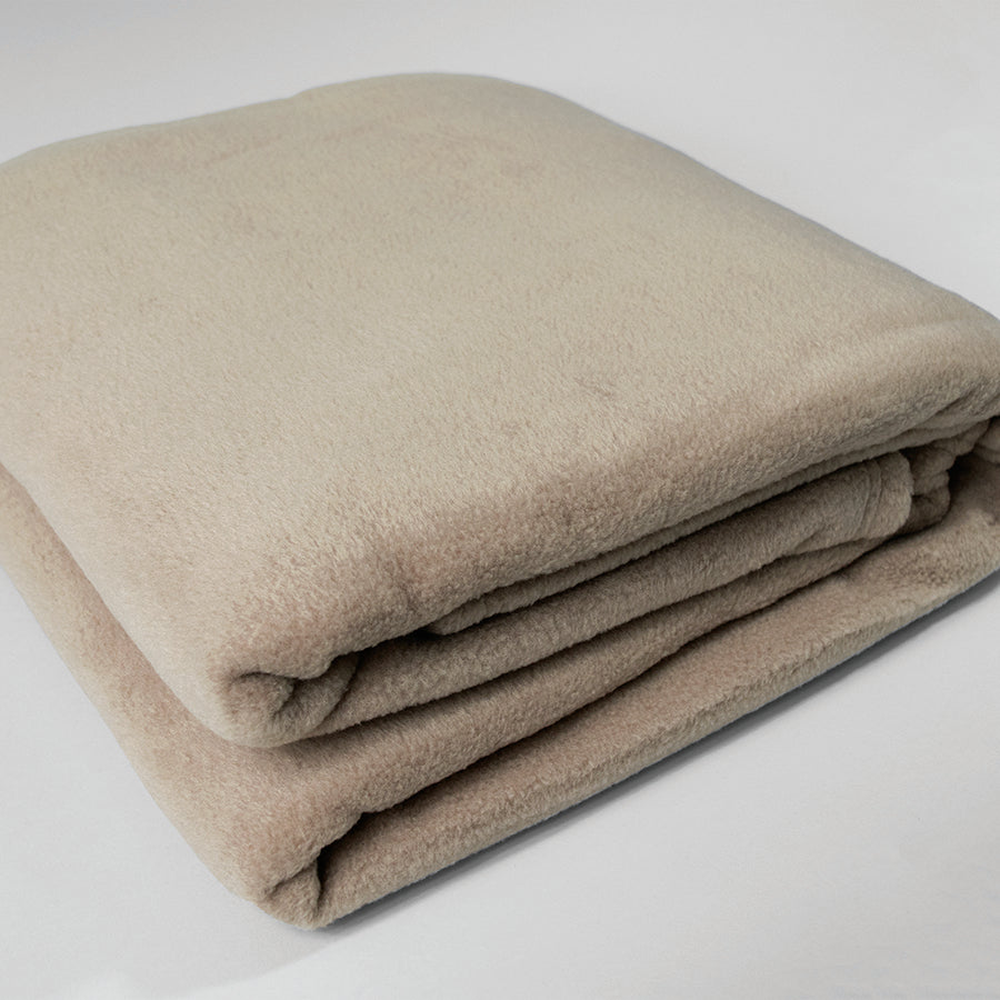 The Calderon Textiles Fleece Blanket Twin, in light beige, is neatly folded and displayed on a white surface. Its color-rich fabric resists shrinking for lasting softness.