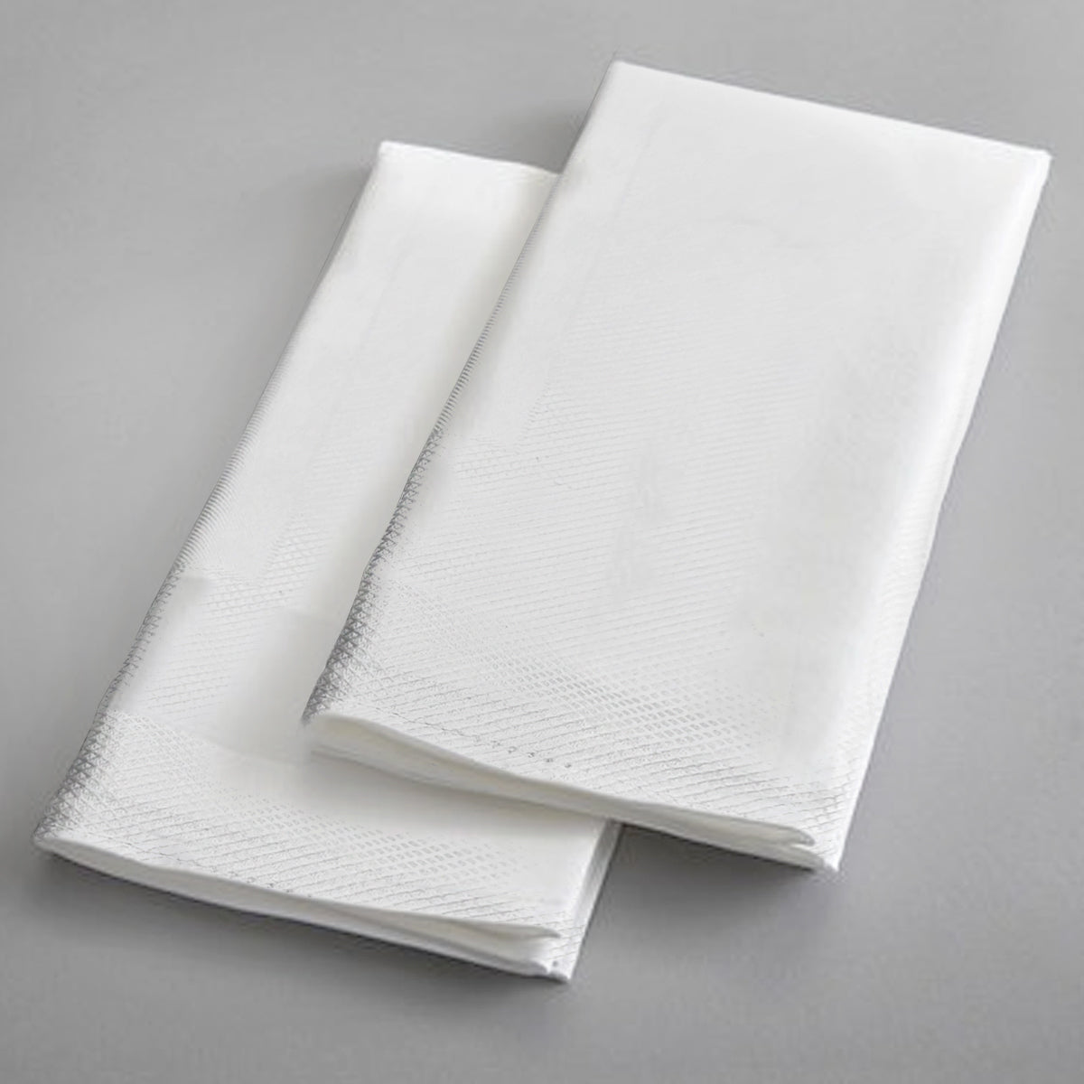 Ganesh Mills Tablecloth - 4 Sided Hemmed White Bird Eye Banquet Table Linen is displayed on a plain grey surface, its elegant white fabric overlapping to evoke the refined look of formal event décor.