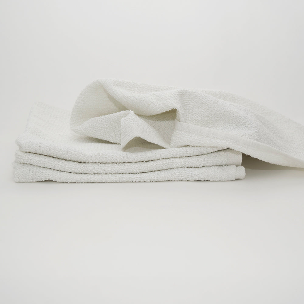 Three white MetroMop Ribbed towels from Calderon Textiles are stacked neatly on a plain white surface, one partially unfolded and draped on top—perfect for quick use in busy environments. The background is simple and uncluttered.