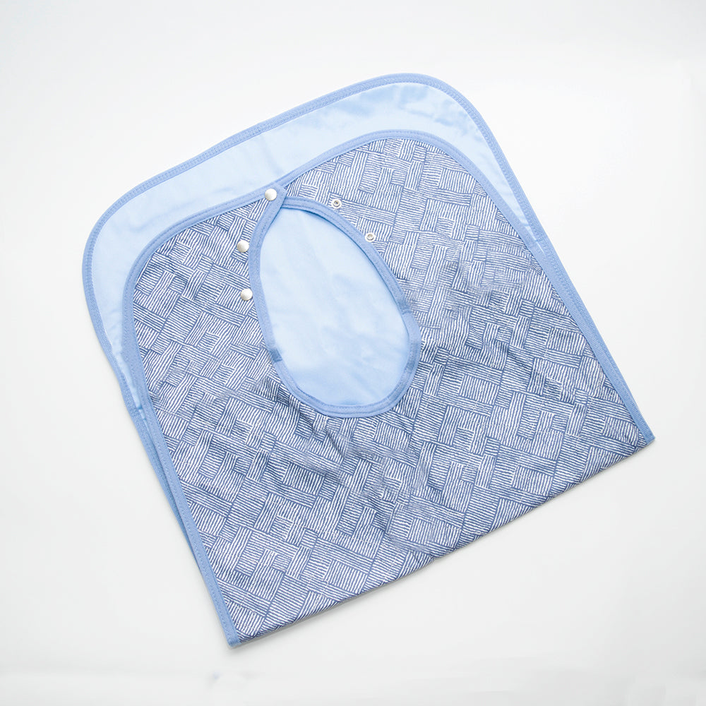 The Calderon Textiles Quilted With Snaps adult bib in blue with a geometric pattern and adjustable snap buttons is displayed flat on a white background.