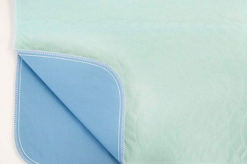 A close-up of Calderon Textiles' Underpad Brushed, Pucker Resistant: light blue and turquoise quilted fabric with wavy stitching and a solid blue underside—ideal for those seeking quality underpads in multiple options.