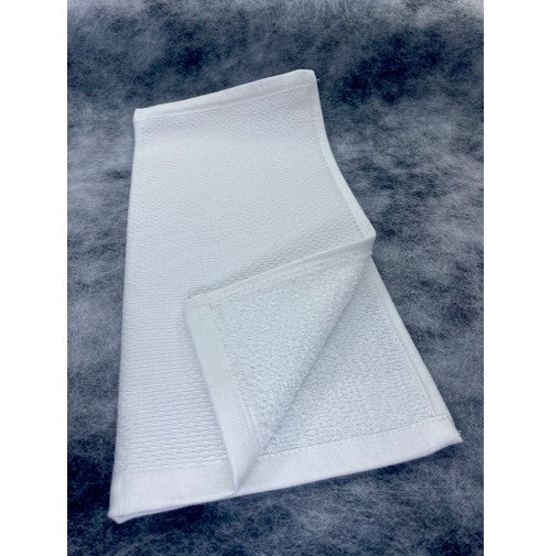 A Ganesh Mills Tea Towel/Hand Towel—terry cloth with back pique design—is neatly folded on a textured gray surface, showcasing its white color, soft fluffy texture, and bordered edges.