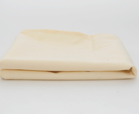 The Prisma Table Cloth Round by Calderon Textiles, a durable and colorfast beige or light cream fabric, is folded and displayed on a white surface with a plain white background.