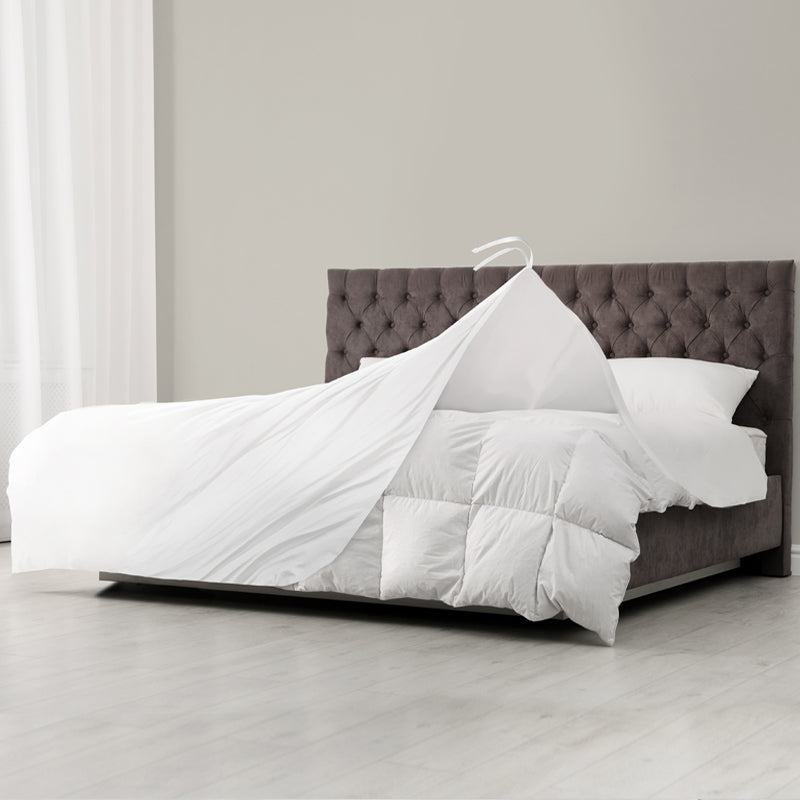 A neatly made bed with a tufted gray headboard, white pillows, and a Ganesh Mills Light Weight Duvet Insert - T210 Fabric with Micro Gel Fiber partially lifted to reveal the mattress underneath.