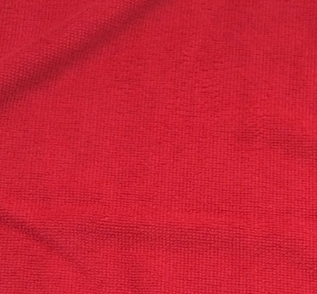 A close-up of a KSE Microfiber Cleaning Cloth shows its textured red surface with subtle folds and a slightly uneven finish.