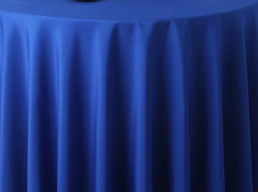 A round table is covered with a smooth Ganesh Mills Oxford Round Table Linen - Multicolor, the fabric cascading in gentle, vertical folds from tabletop to floor.