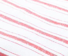 A close-up of the Intralin Glass Towel - Herringbone Kitchen Towel shows white 100% cotton fabric with red horizontal stripes in varying thickness, evenly spaced across the surface.