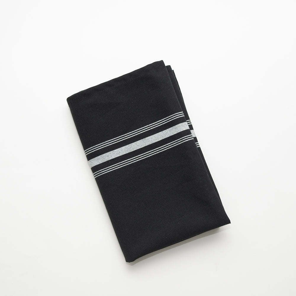 The Calderon Textiles Prisma Napkin, Inverse Stripe, features neatly folded black fabric with two white stripes near the edge, displayed on a white background and known for its impressive durability and colorfastness.