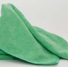 A Calderon Textiles Microfiber Cleaning Cloth in green, resembling microfiber bar mops, is loosely folded on a plain white surface.