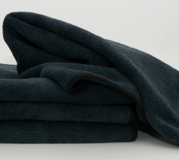A close-up shows three neatly folded Calderon Textiles Microfiber Cleaning Cloths stacked on a light surface, with one draped over the top—perfect for everyday cleaning and reducing laundering costs.