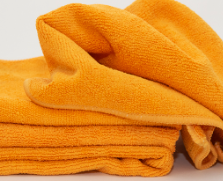 A close-up of two bright orange Calderon Textiles Microfiber Cleaning Cloths, one folded and one draped over it—ideal for bars aiming to reduce laundering costs.