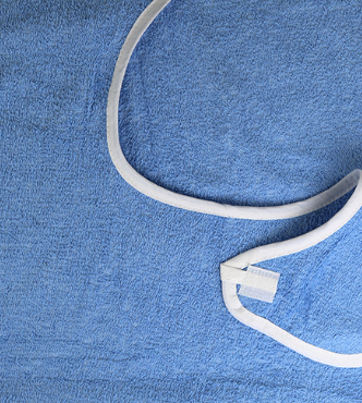 A close-up of the KSE Premium Adult Terry Bib / Clothing Protector in blue terry cloth with a white trim and metal snap closure, spread out flat.