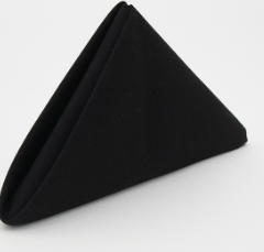 The Prisma Napkin by Calderon Textiles, in black and made with Color Lock dyeing for lasting vibrancy, is folded into a neat triangle and stands upright on a white surface.