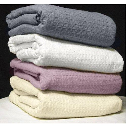 Four Santa Clara Cotton Thermal Blankets by Intralin, featuring a honeycomb pattern, are stacked in gray, white, lavender, and cream against a dark background.