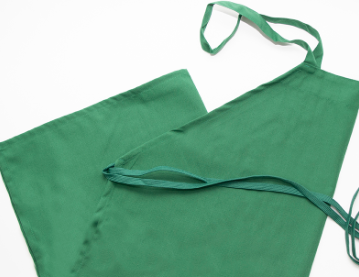 A Prisma Bib Apron by Calderon Textiles in green polyester is laid flat on a white surface, showing its neck loop and waist ties for superior comfort.